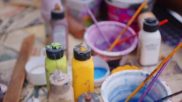 Close-up of used paint cans with paintbrushes and water cans on table with newspaper