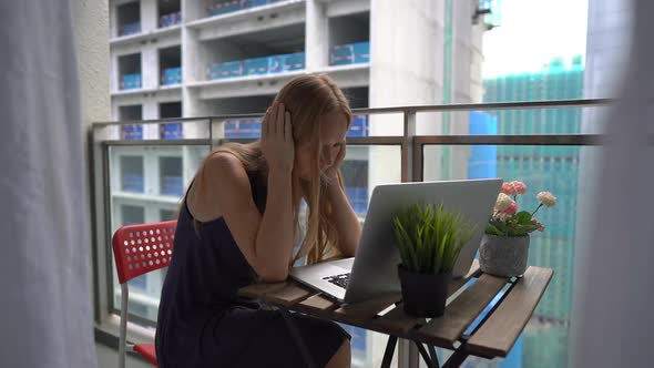 Slowmotion Shot of a Young Woman Sitting on a Balcony with a Notebook and Suffering From a Loud