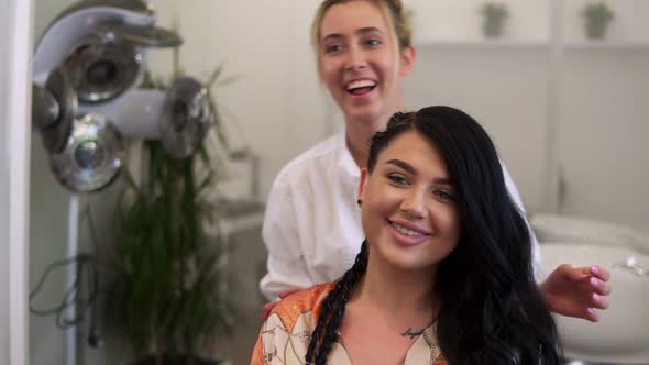 A Brunette Woman in a Salon Sitting in Front of Mirror and Hairdresser is Fixing Her Hair with Hands