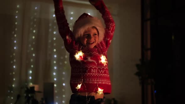 Excited Christmas Boy Jumping Dancing in Santa Hat at Home Evening