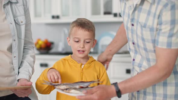 Portrait of Beautiful Little Boy Picking Sea Roach From Meal Plate with Mom and Dad at Home Backdrop