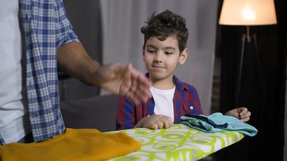 Son Helping Dad To Fold Ironed Clothes at Home