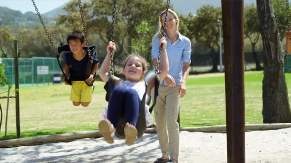 Trainer and schoolkids pushing their friends on swing in playground