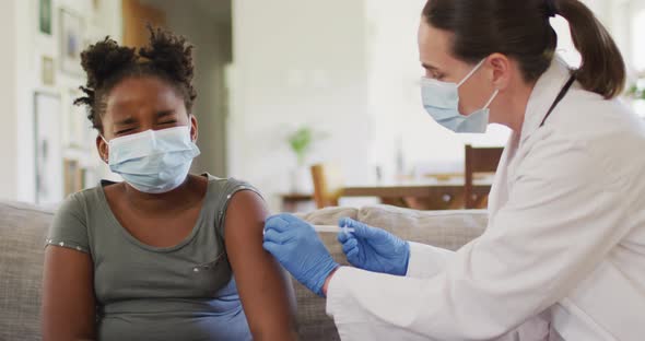 African american girl and caucasian female doctor wearing face masks, vaccinating