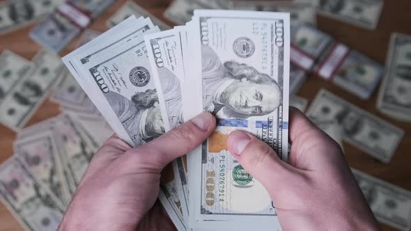 Dollars in Male Hands on Background of Table with Money