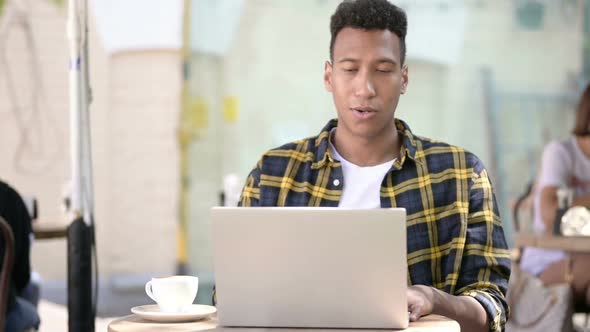 Online Video Chat on Laptop By Young African Man Outdoor Cafe