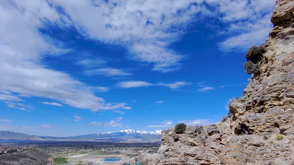 Flying close the the side of a cliff then reveal a wide urban valley with snow-capped mountains on t