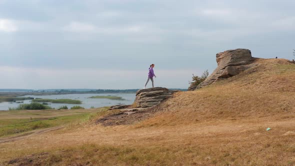 A Girl is Doing Fitness on a Hill on the Lake Shore