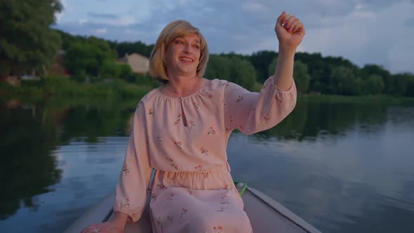 Smiling Caucasian Trans Woman in Pink Dress Admiring Golden Sunset Sitting in Boat on Summer Lake