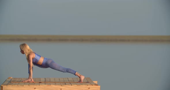 Sexy Woman in Blue Sportswear is Doing Yoga During Sunset on the Lake