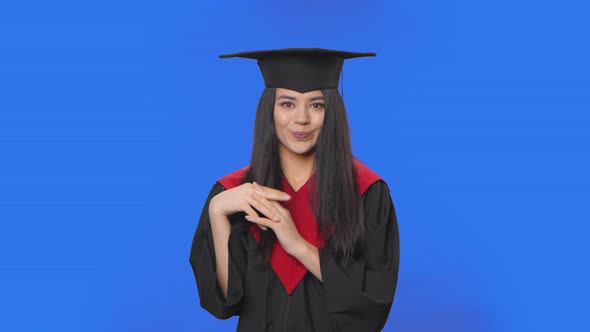 Portrait of Confused Female Student in Graduation Costume Saying Oops Shrugging and Biting Lips