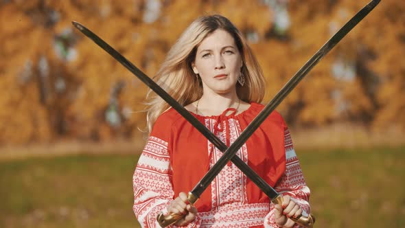 Feisty Woman in Red Clothes Standing on the Field with Her Swords Crosswise