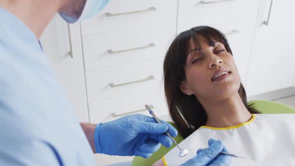 Caucasian male dentist with face mask examining teeth of female patient at modern dental clinic