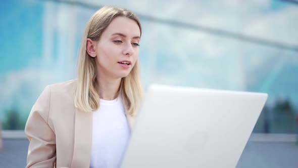 young business woman sitting on the sidewalk and working on laptop