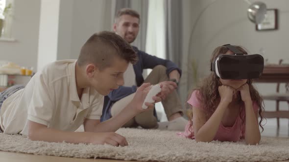 The Boy and Girl Laying on the Floor on the Fluffy Carpet Using Virtual Reality Glasses, Father