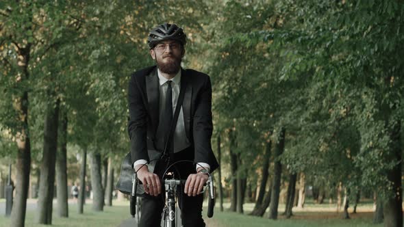 Businessman Riding a Bike in City Park Wearing Suit and Helmet Front View