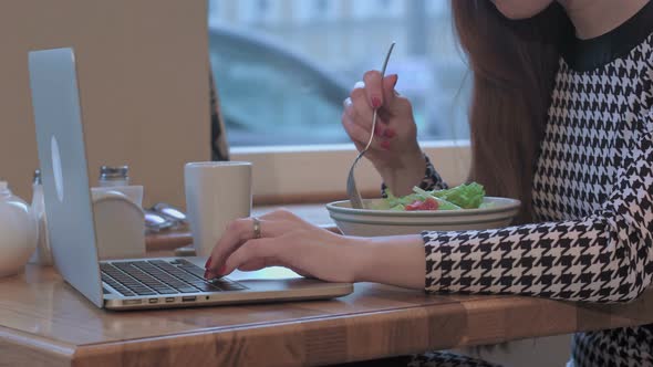 Arms of Young Businesswoman Using a Laptop for Work. She Is Sitting at the Table in Cafe and Eating