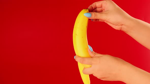 Woman's Hands Peeling Banana on Red Background