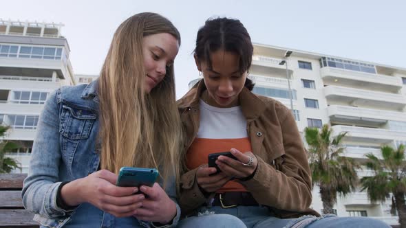 Front view of a Caucasian and a mixed race girl using their phones