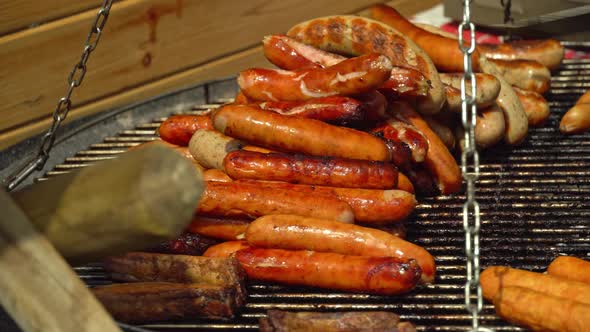 Chef flips sausages Bratwurst roasting with cooking tongs. BBQ grilling frankfurt beef sausage