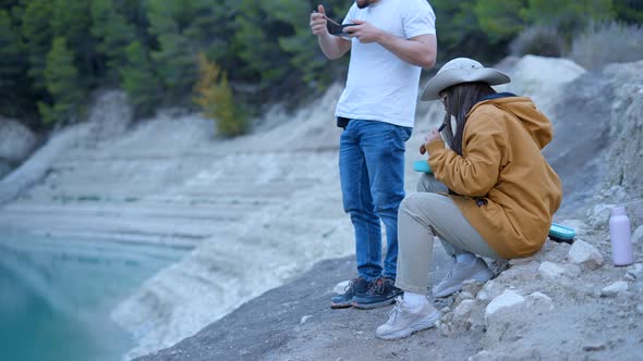 Young Couple Eat From Lunch Boxes in Stony Nature Man Uses Phone