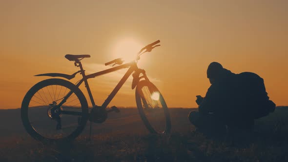 Silhouette Cyclist Use Mobile Phone on a Mountain at Sunset.