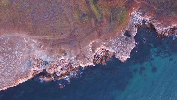Top down aerial view of waves splash against rocky seashore, background. Flight over high cliffs of