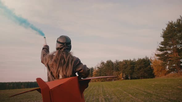 Little Pilot Girl Running in Fun Plane Costume with Color Smoke in Hand on Amazing Autumn Sunset