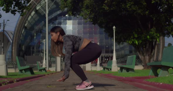 Low angle view of a young female performing burpees at a park with a biulding in the background