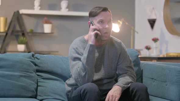 Angry Casual Man Talking on Smartphone on Sofa