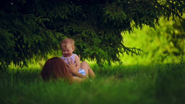 Mom with a child have fun lying in a park under a tree.