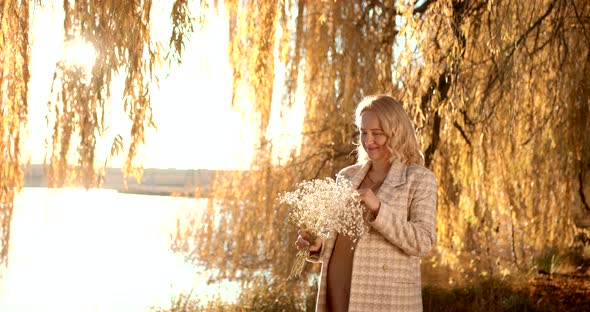 Pregnant Blonde Woman with a Bouquet on the Shore of the Pond