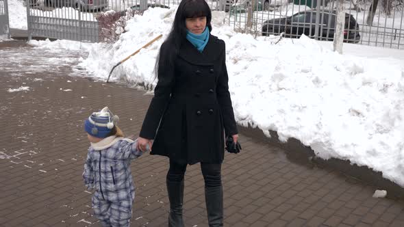 Mother Walks With Her Child In City. Snowy Winter