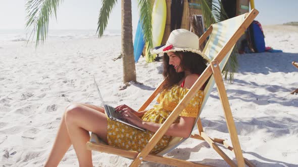 Caucasian woman sitting on a sunbed and using his laptop on the beach