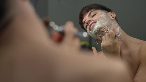 Reflection of Young Man Shaving Chin in Slow Motion at Home in Bathroom