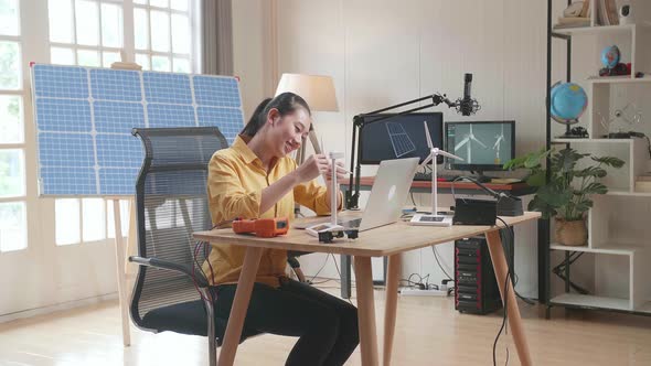 Asian Woman Assemble The Wind Turbine While Working With Laptop Next To The Solar Cell At The Office