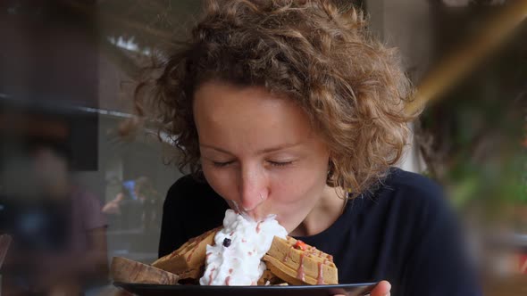 Happy Pretty Curly Woman Biting Cream From the Belgian Waffles with Berries and Syrup Enjoying Her