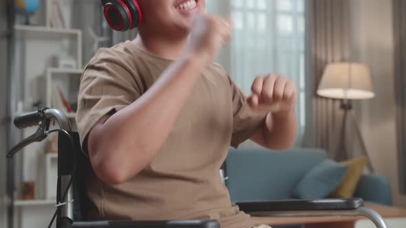 Close Up Young Asian Boy Sitting In A Wheelchair Listening To Music With Headphones And Dancing