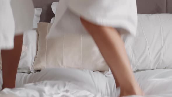 Joyful Young Couple in Bathrobes Jumps on Large Bed