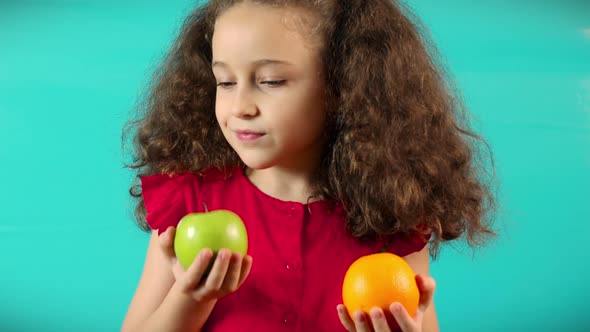 Cute Child on Turquoise Background of Holding a Green Apple and Orange and Choice Healthy Eating