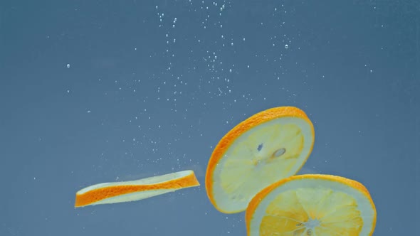 Slices of Orange Entering Into Water Against White Background