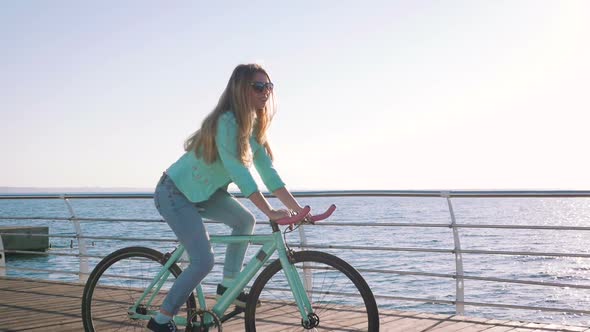 Young Stylish Woman Cyclist Enjoying Fixed Gear Bike Riding Outdoors at Sunrise Near the Sea