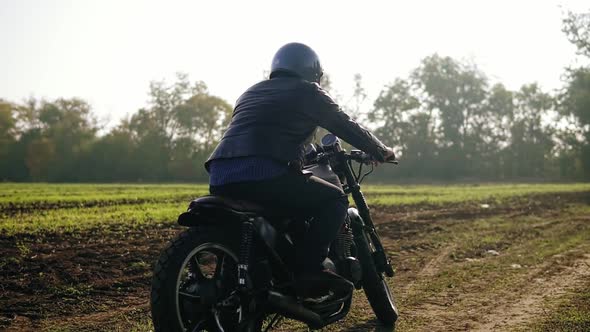 Back View of a Man in Helmet and Leather Jacket Coming Up to His Bike and Starting the Engine While