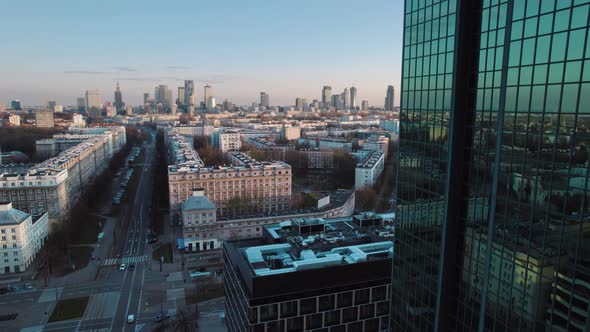 Drone flying backwards revealing Warsaw in Poland polish cityscape through glassy skyscrapers at sun