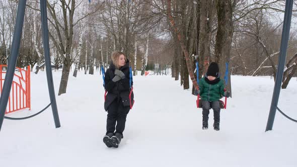 Mom and Son Ride on a Swing in a Winter Park