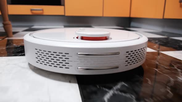 The Robot Vacuum Cleaner Cleans in the Modern House on the Tiles Floor at Kitchen