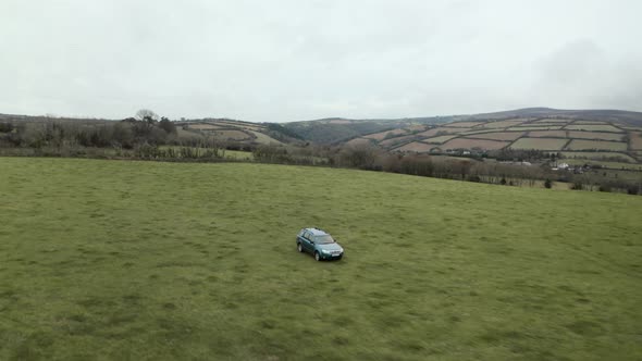 Dolly back aerial drone shot of farmer driving 4x4 around an empty field