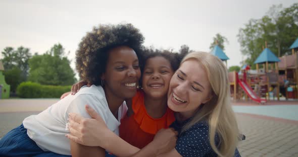 Multiethnic Lesbian Couple and Adopted Little Daughter Hugging on Playground