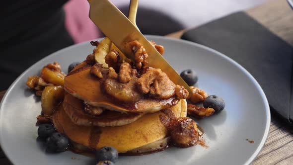 Close Up of Hand Cutting Stack of Vegan Pancakes Decorated with Berries in Nuts