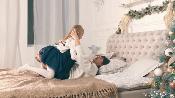 Happy Smiling Mother with Daughter Sitting on Her Legs and She Lifts Her Up